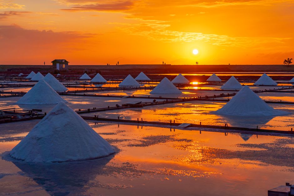A farmer raking crystallized salt into a pile at Jingzaijiao's tile-paved salt pans