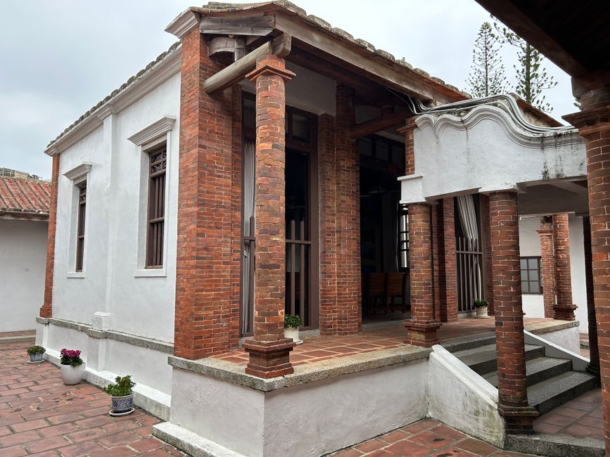 Fachada ornamentada de una mansión de estilo occidental de principios del siglo XX con columnas en la Aldea Shuitou, Kinmen, junto a una casa tradicional de ladrillo rojo