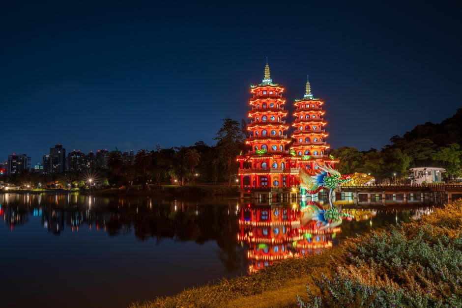 The twin Dragon and Tiger Pagodas of Lotus Pond viewed from the water's edge, their colorful towers reflected in the still surface