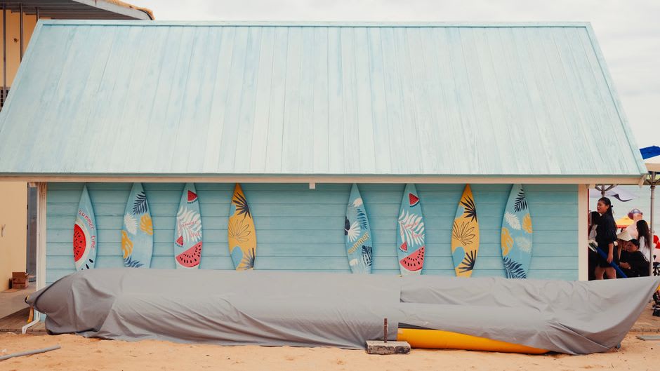 Une rangée de planches de surf appuyées contre une cabane en bois près de la plage de Dulan au lever du soleil