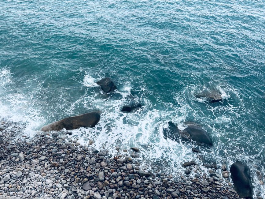Waves crashing against the pebble shoreline at Qixingtan Beach with mountains in the background