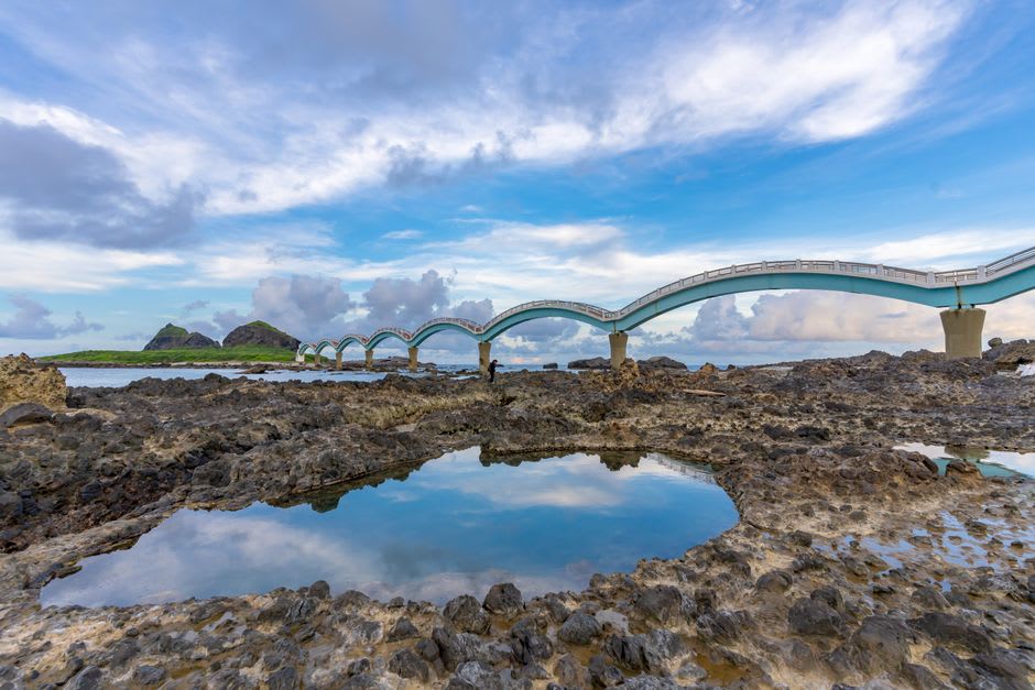 The curving stone arches of Sanxiantai bridge reflected in shallow turquoise water