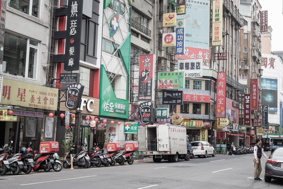 A crowded pedestrian crossing in Ximending at dusk, illuminated signage stacked several storeys high above the street