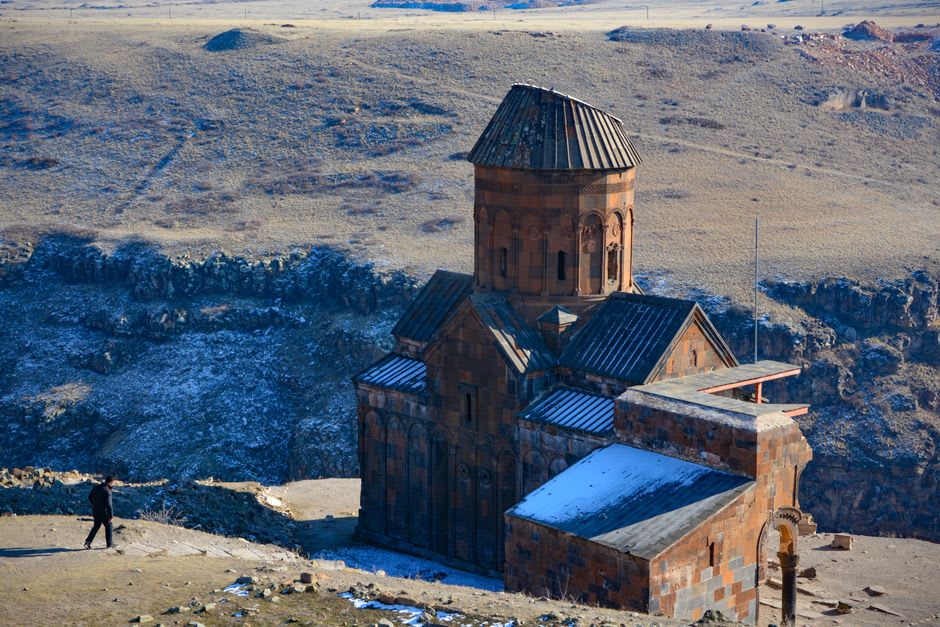 The roofless ruins of Ani's cathedral standing in the open grassland with the border river gorge beyond
