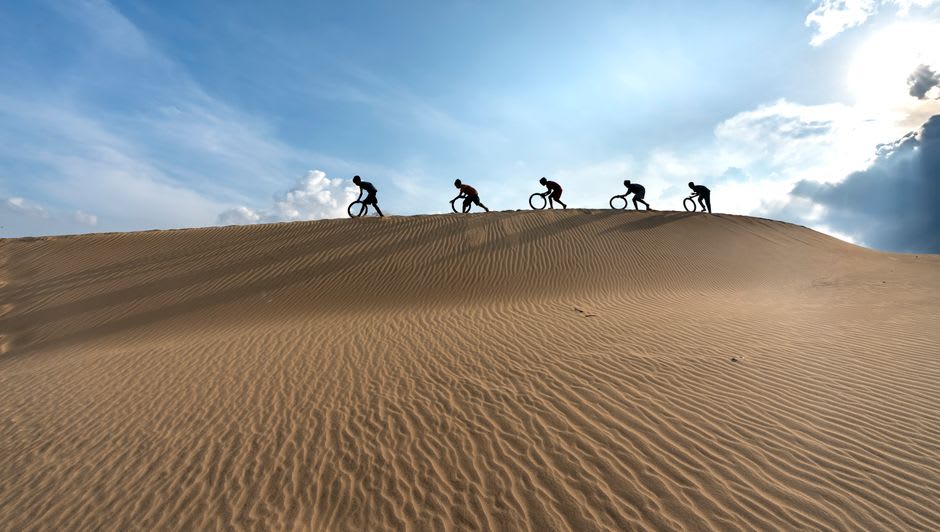 Cyclist riding along a paved desert track near Al Qudra Lake with dunes on either side