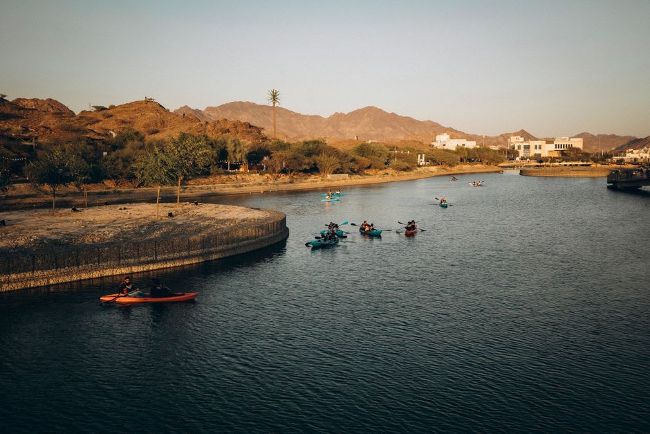 Kayaker paddling across the turquoise Hatta Dam reservoir with brown mountain peaks rising behind