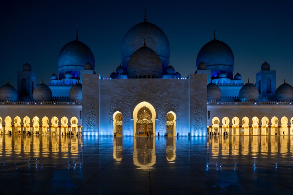 Jumeirah Mosque reflected in a still pool at night with its facade lit gold