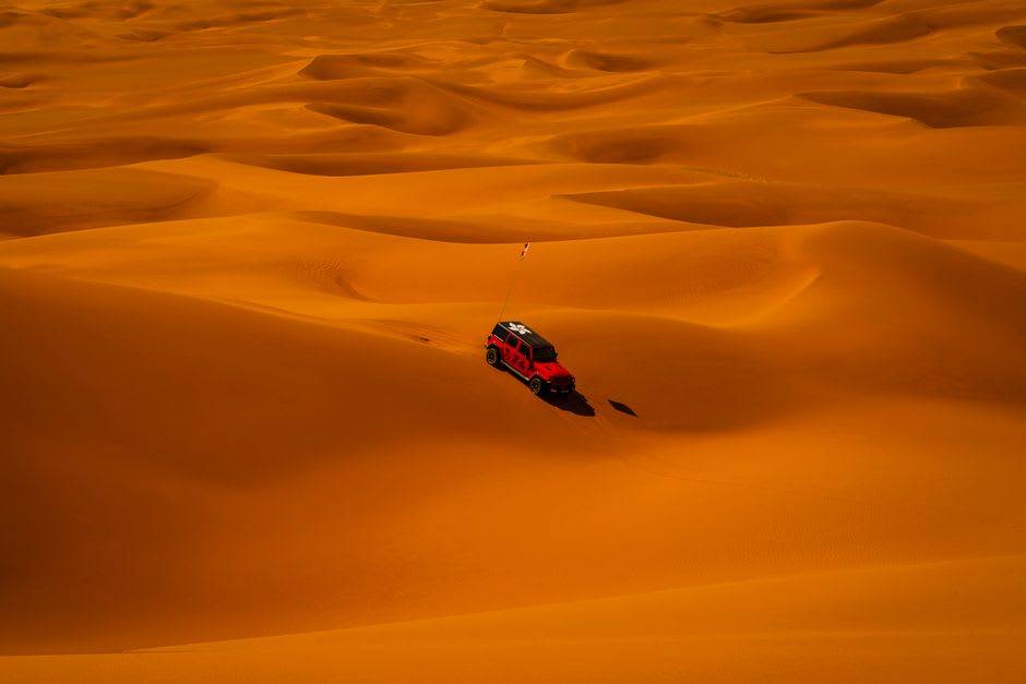 A dune buggy kicking up red sand against the Mleiha desert landscape