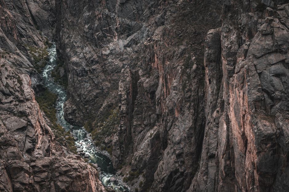 A viewer at a railing peering into an extremely deep, narrow, dark-walled canyon