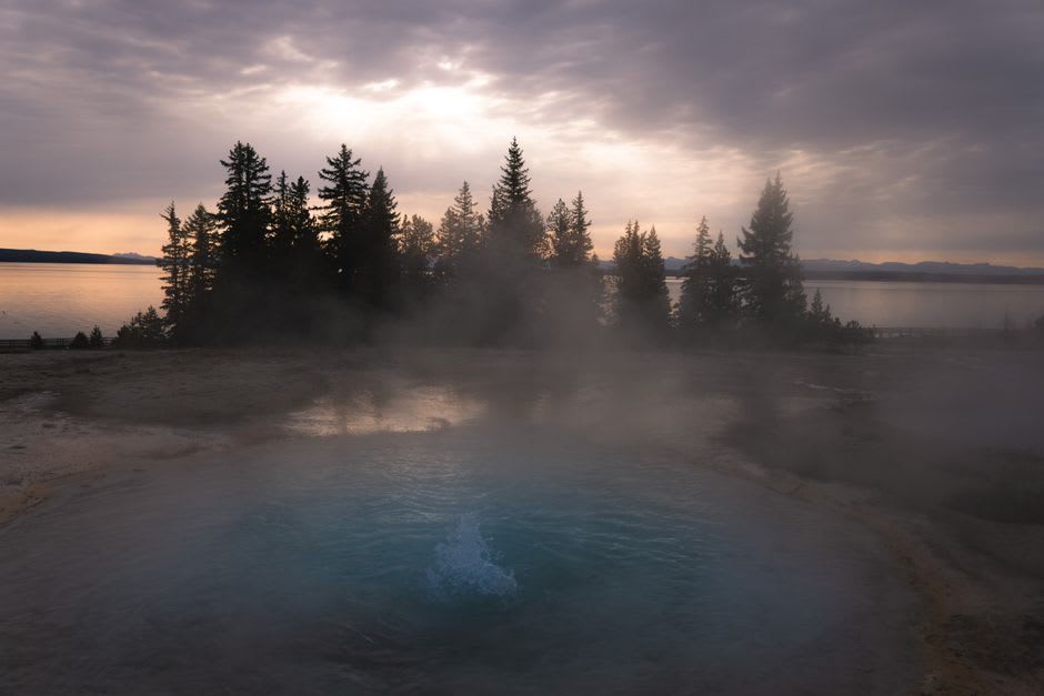 Steam rising from a hot springs soaking pool at dusk near Caliente, Nevada with canyon walls behind
