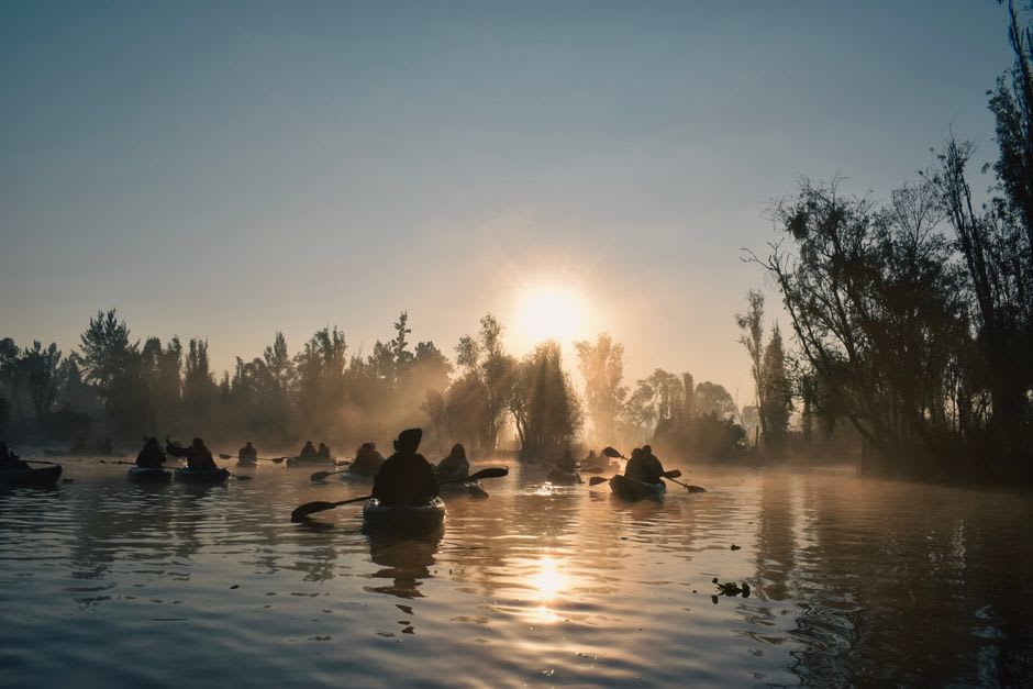 Kayaks paddling across the calm water of Ninigret Pond at sunrise in Charlestown, Rhode Island