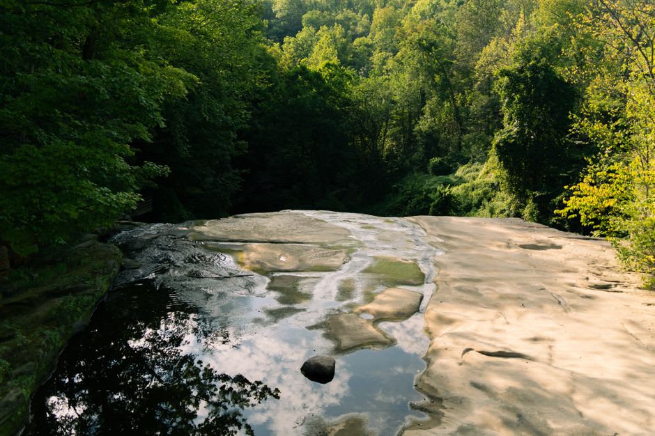 A tall multi-tiered waterfall dropping over layered sandstone into a fern-lined pool