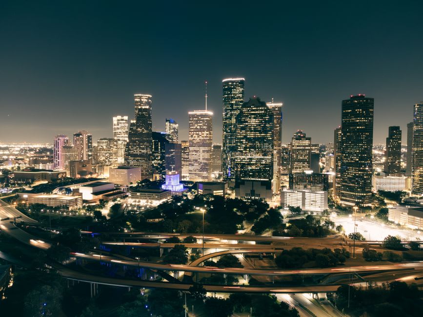 The still reflecting pool and live oaks of Hermann Park with downtown beyond