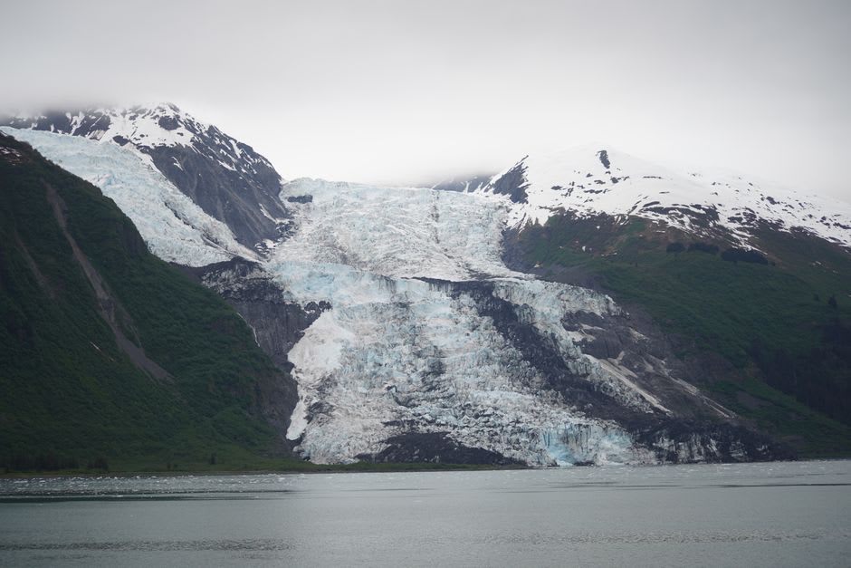 A wall of cracked blue glacier ice meeting the sea at the head of a fjord