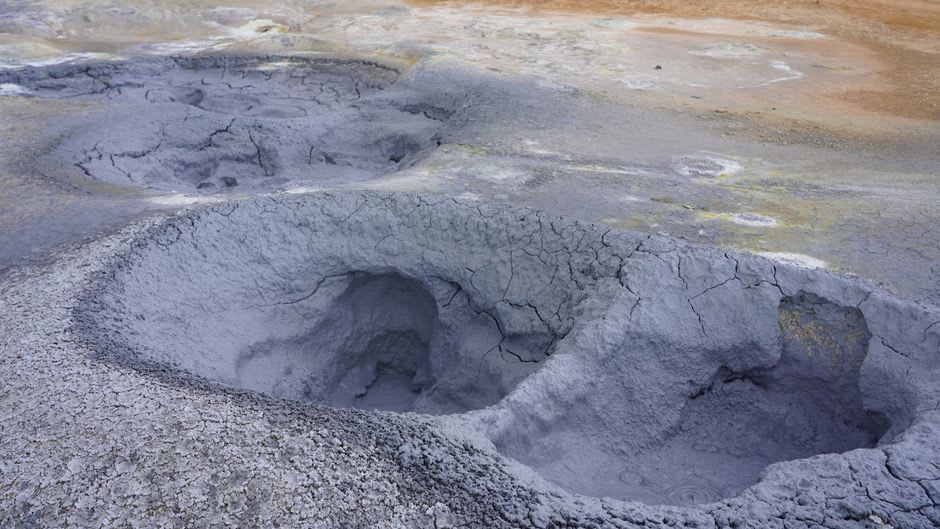A boardwalk winding through a steaming hydrothermal basin of boiling blue pools and pale earth