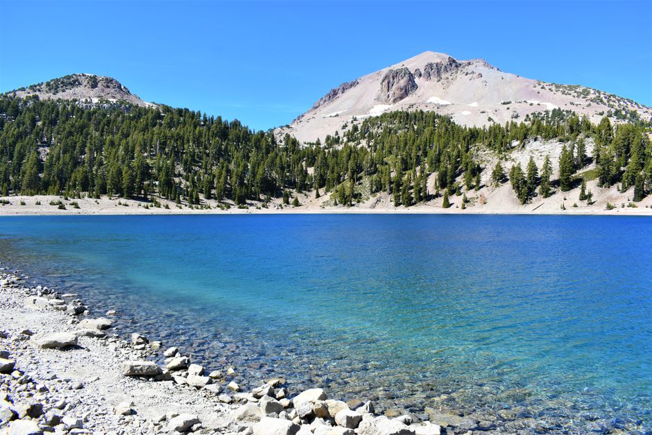 A still alpine lake at dawn mirroring a snow-streaked volcanic peak with pine forest around