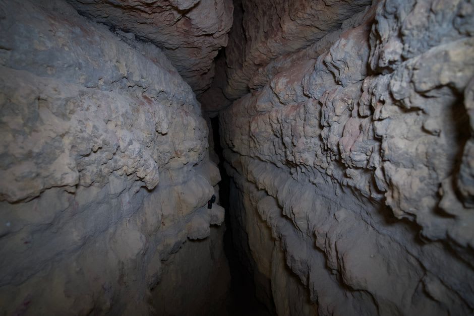 A narrow winding limestone passage inside Mammoth Cave, walls worn smooth and lantern light glinting off the stone