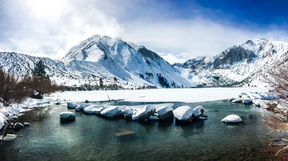 The still blue-green water of one of the Mammoth Lakes reflecting jagged Sierra peaks and pine forest