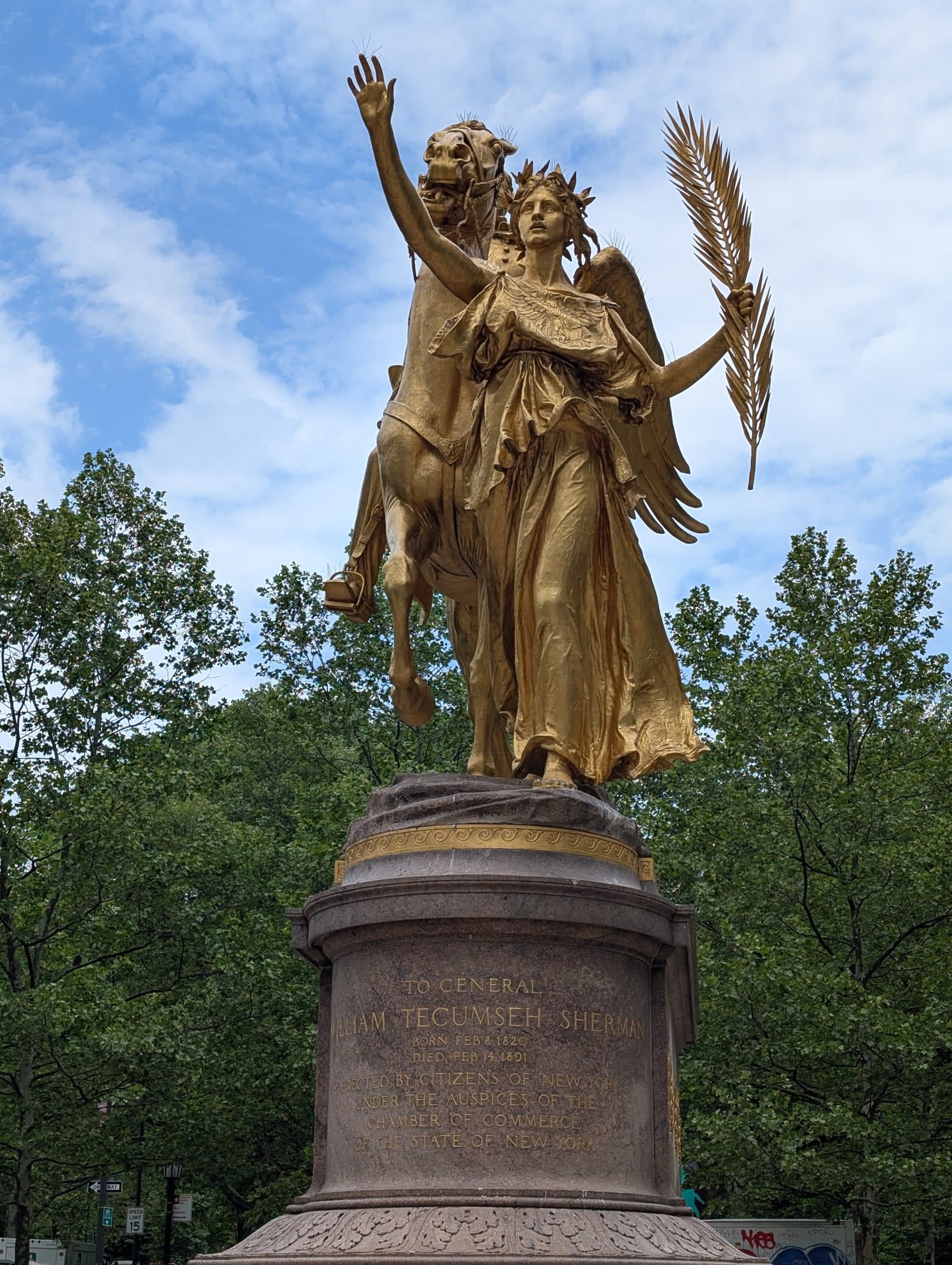 The General Sherman Monument at Grand Army Plaza — Augustus Saint-Gaudens' gilded equestrian group: Victory leading Sherman's horse, wings spread, arm raised against a sky of early-May clouds, the trees of Central Park beginning behind it