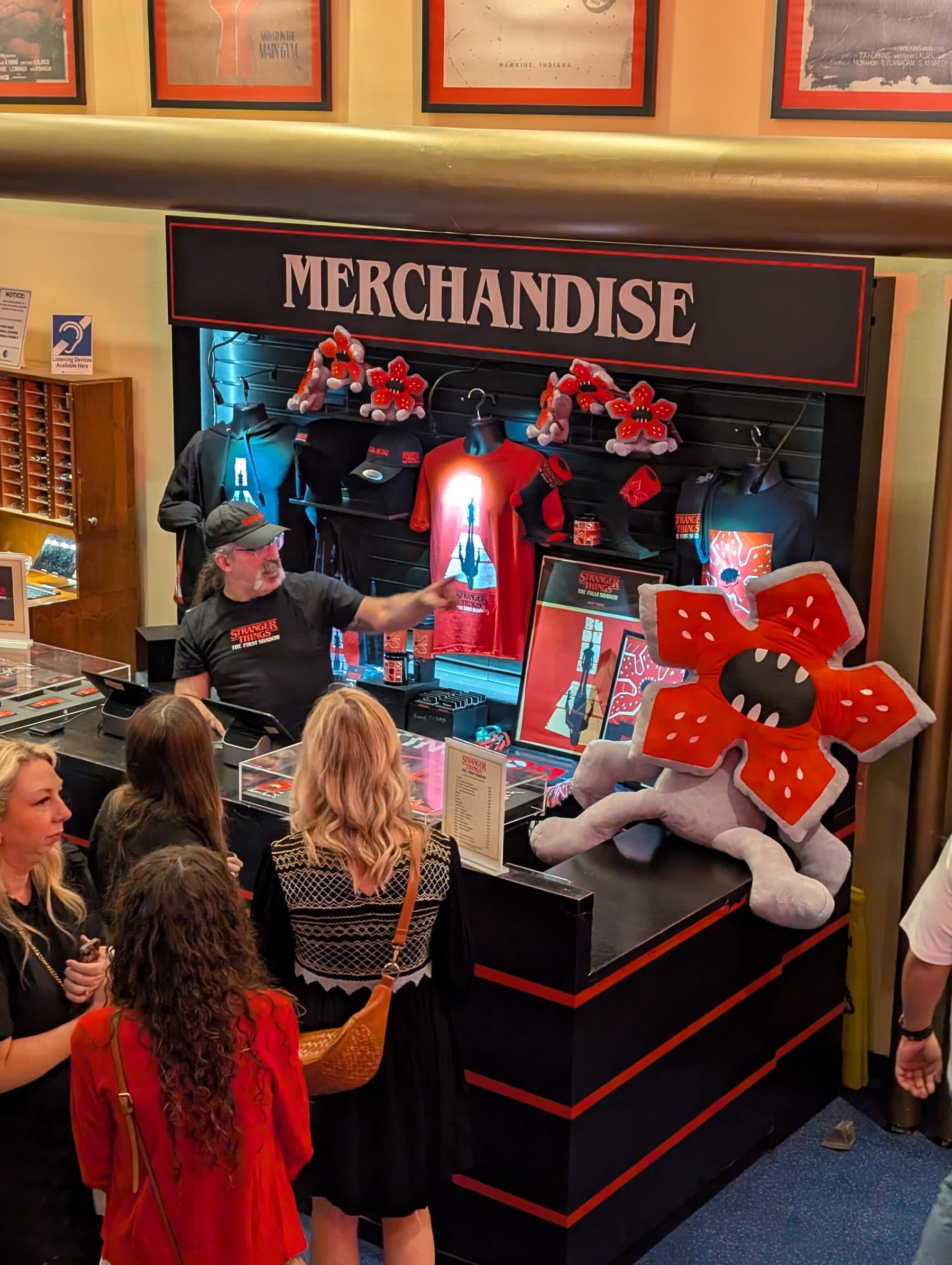 The Stranger Things merchandise stand inside the Marquis Theatre lobby — a Demogorgon plush toy prominently displayed, Stranger Things t-shirts and caps behind the counter, audience members browsing before the show