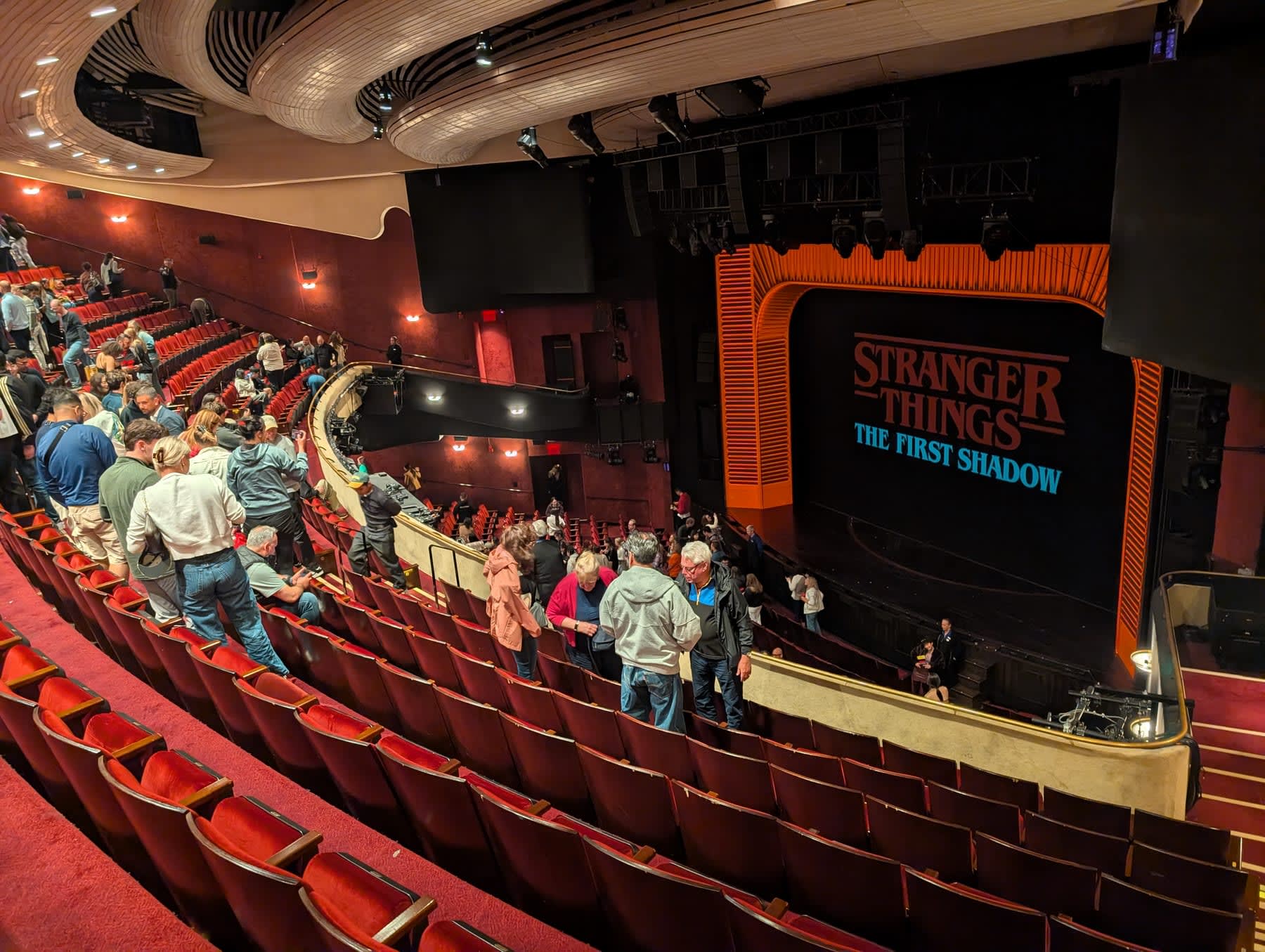 Inside the Marquis Theatre as the audience begins to leave — "Stranger Things: The First Shadow" displayed on the proscenium arch above the stage, red and gold theatre architecture, rows emptying