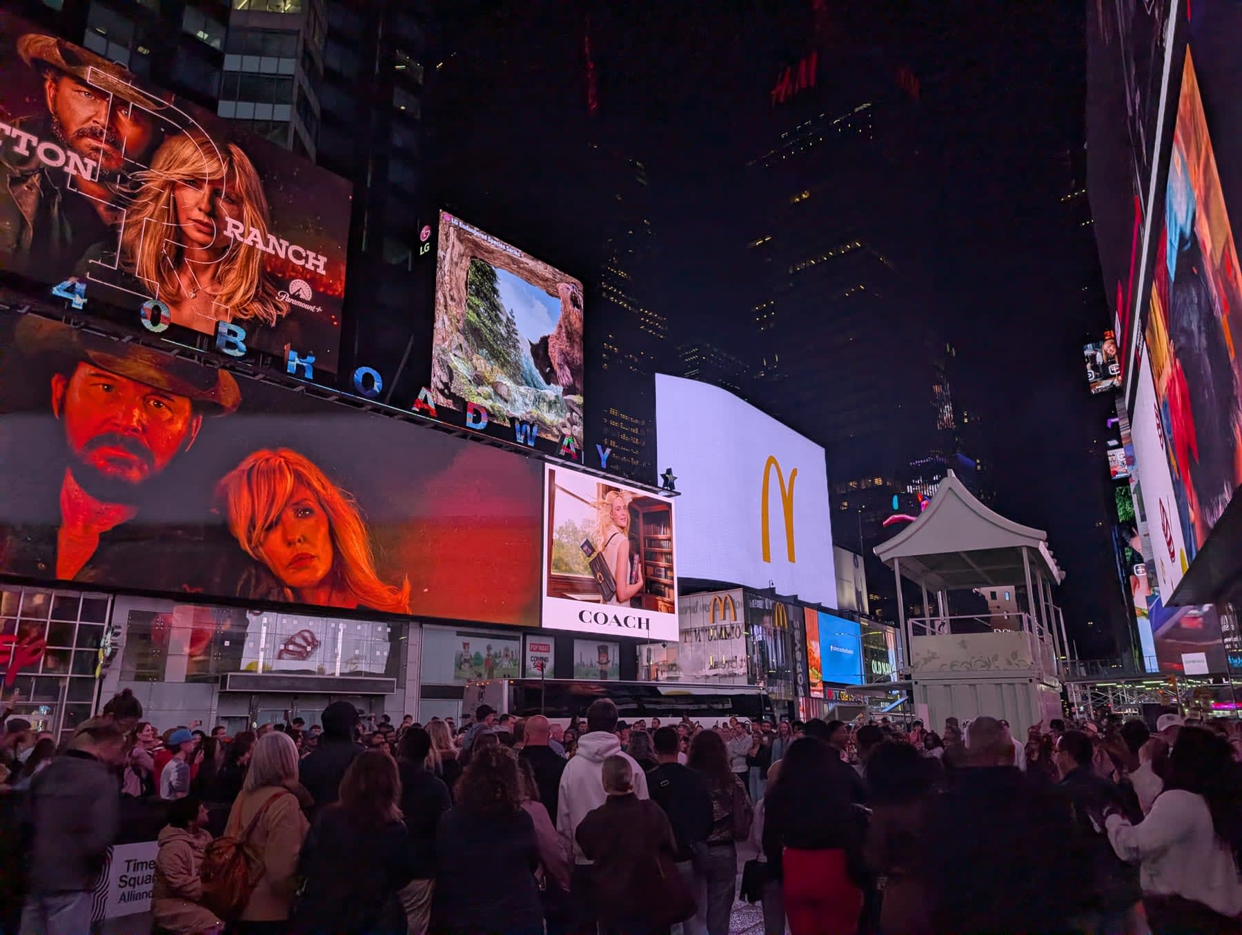 Times Square at 2am — billboards for the Yellowstone Ranch series, Coach, and McDonald's blazing in the darkness, crowds gathered below, the square reduced to its essential elements: light and people and the refusal to be quiet