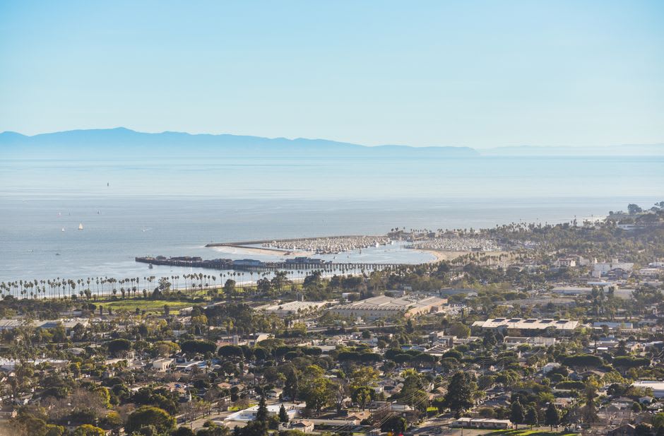 Stearns Wharf reaching out into Santa Barbara harbor at golden hour, with the mountains glowing purple behind the palm-lined waterfront