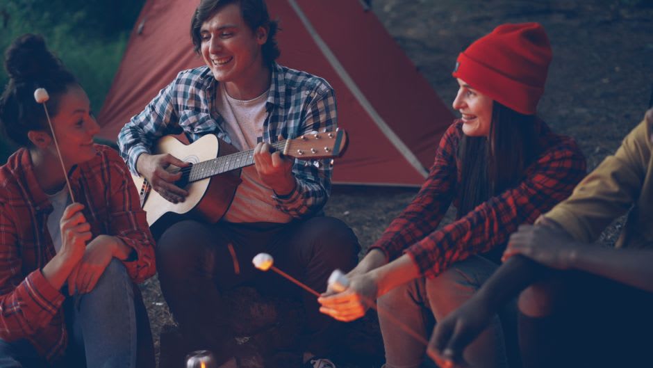 A group of musicians playing acoustic guitars around a campfire at night during the Walnut Valley Festival near Winfield, Kansas