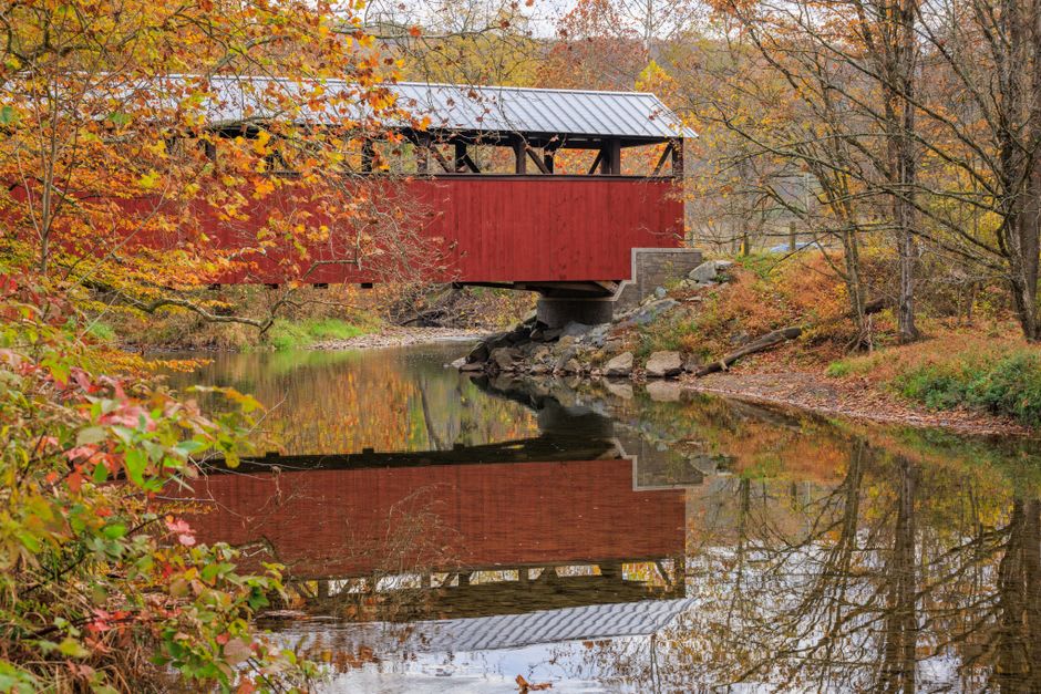 A weathered red covered bridge spanning a creek in the Madison County countryside near Winterset, Iowa