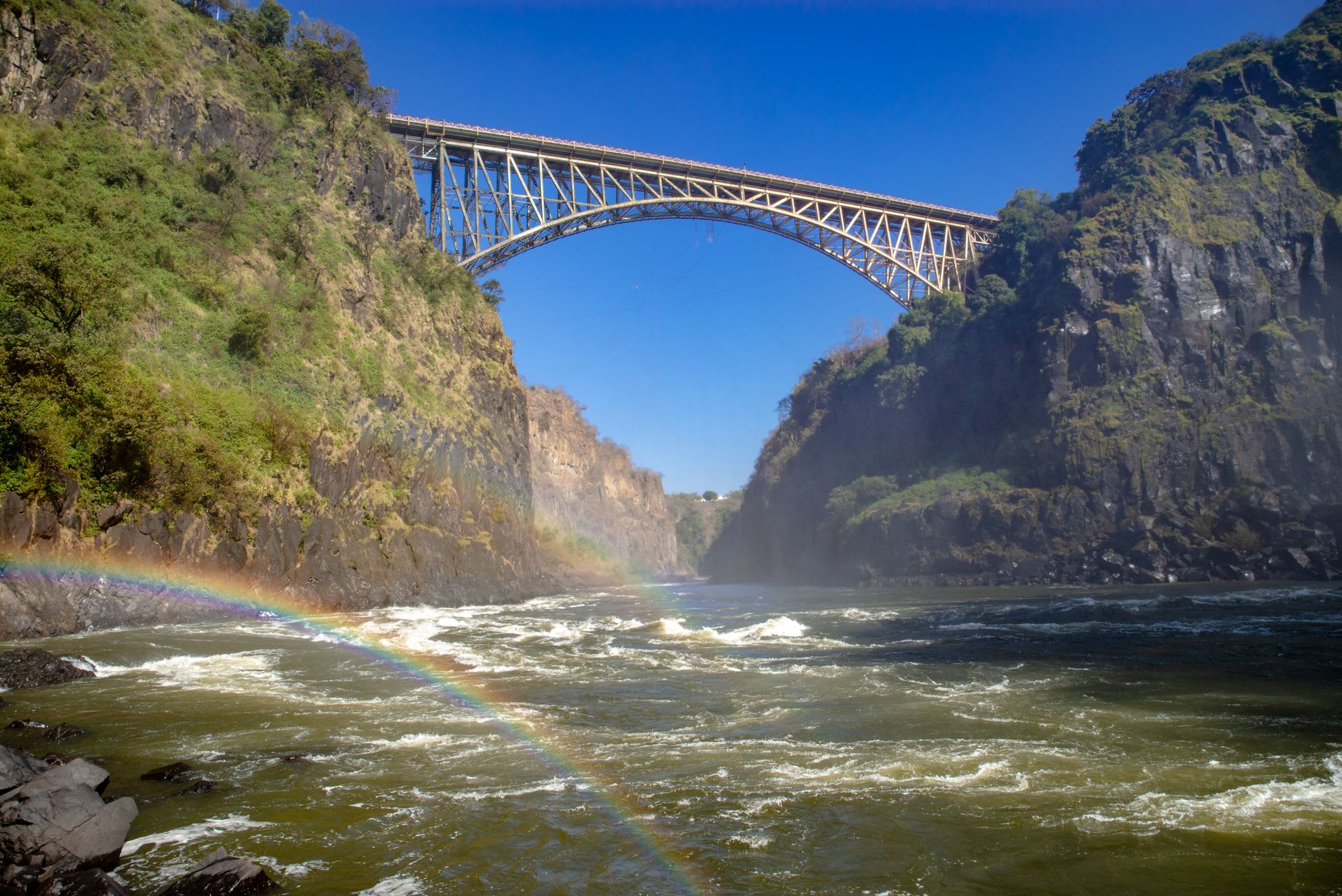 The pedestrian walkway across Victoria Falls Bridge with the steel arch above and mist in the gorge below