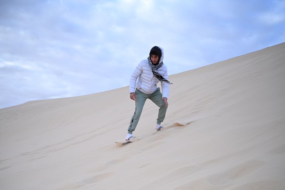 A sandboarder speeding down a steep white dune near Lancelin, Western Australia