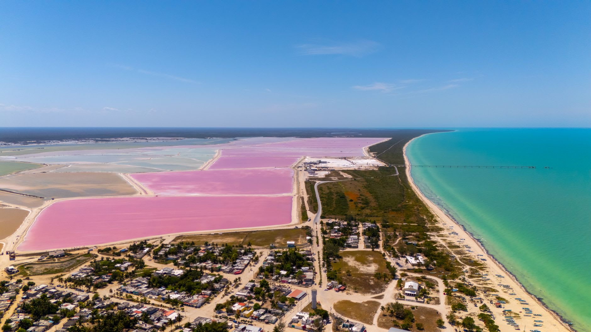 Vivid pink salt-evaporation ponds beside white salt mounds under a blue sky