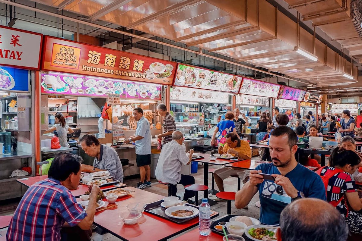 A bustling hawker centre with diners at communal tables and steam rising from food stalls