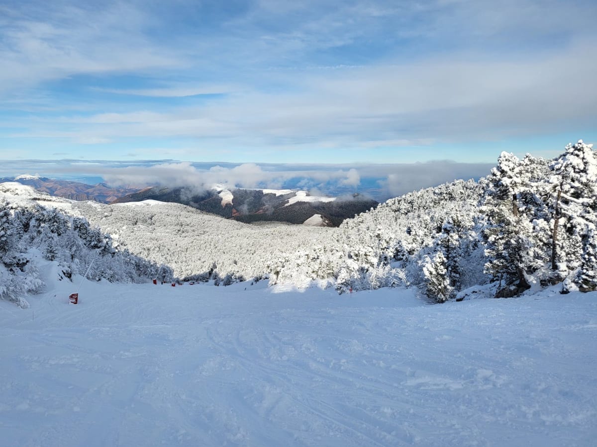 Esquiadores en una amplia pista roja en Grandvalira con el valle andorrano visible muy abajo a través del aire frío de montaña