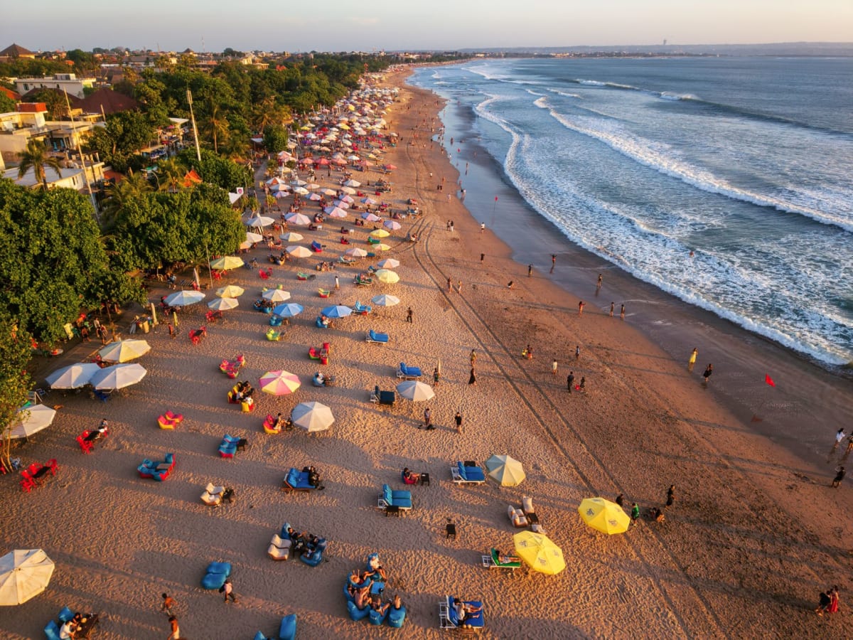 Tôt le matin sur la plage de Seminyak, femmes balinaises portant des offrandes pour les temples vers les vagues déferlantes