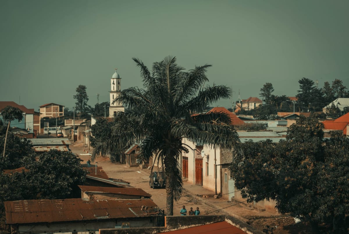 Makamba's central market on a weekday morning — vendors under blue tarpaulins, baskets of dried goods, a boda-boda parked at the edge of the crowd