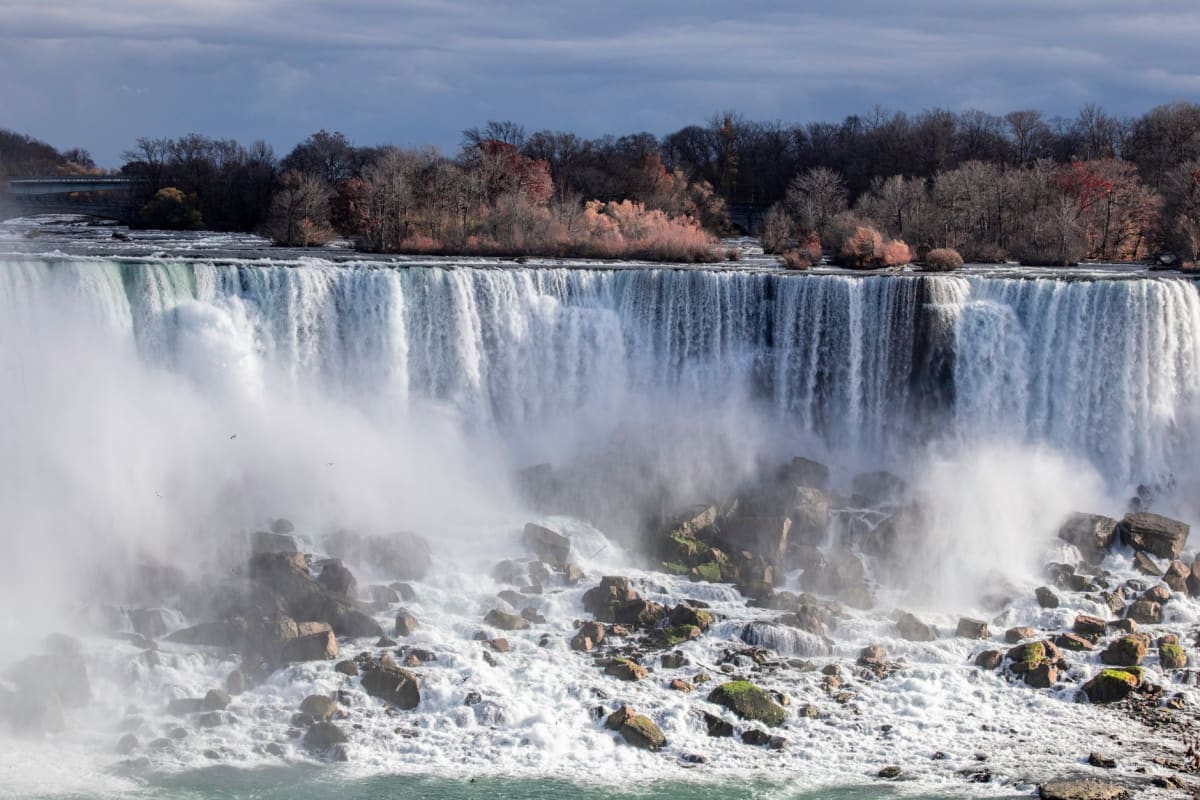 Turistas con ponchos azules apiñados a lo largo de una pasarela neblinosa con las cataratas Herradura rugiendo justo detrás de ellos.