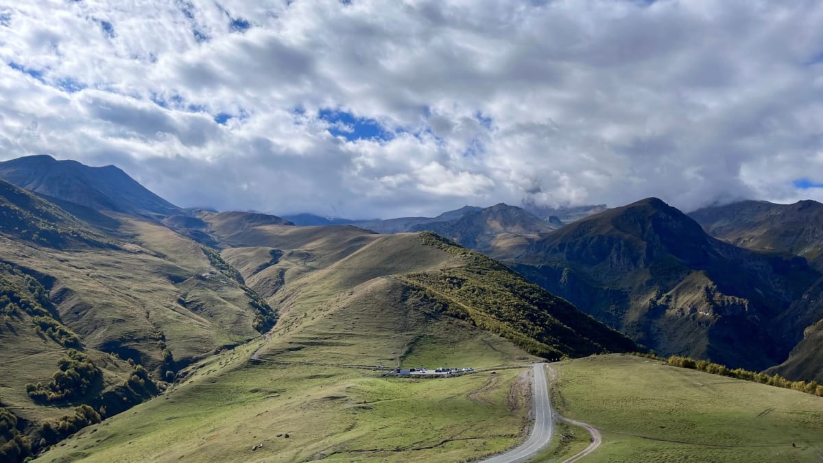 High Tusheti pasture at golden hour with sheep on a distant hillside and the spine of the Greater Caucasus catching the last light