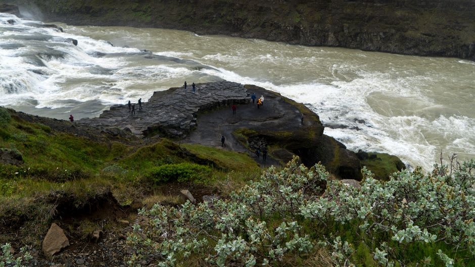 Excursionistas de pie en un saliente de roca mirando hacia una profunda cuenca de cascada al amanecer