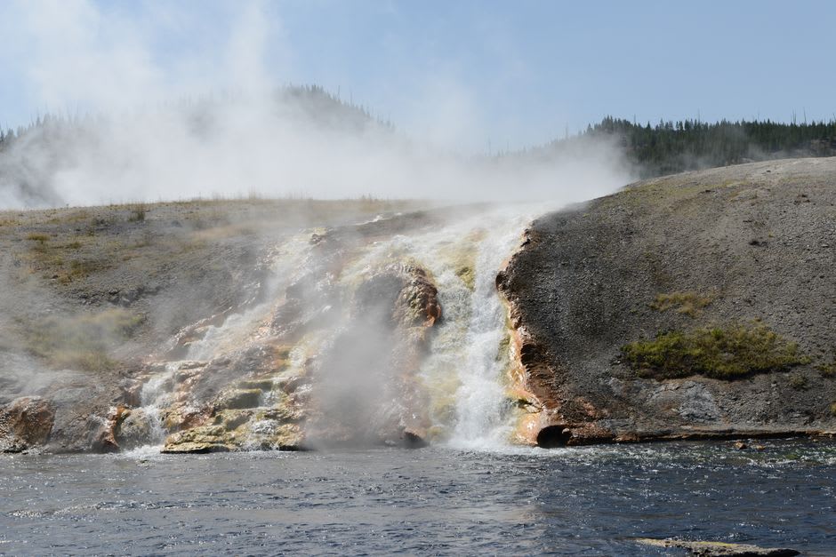 Vapor elevándose de la cascada termal principal de Ma'in al estrellarse en la piscina de abajo, paredes de roca negra a ambos lados
