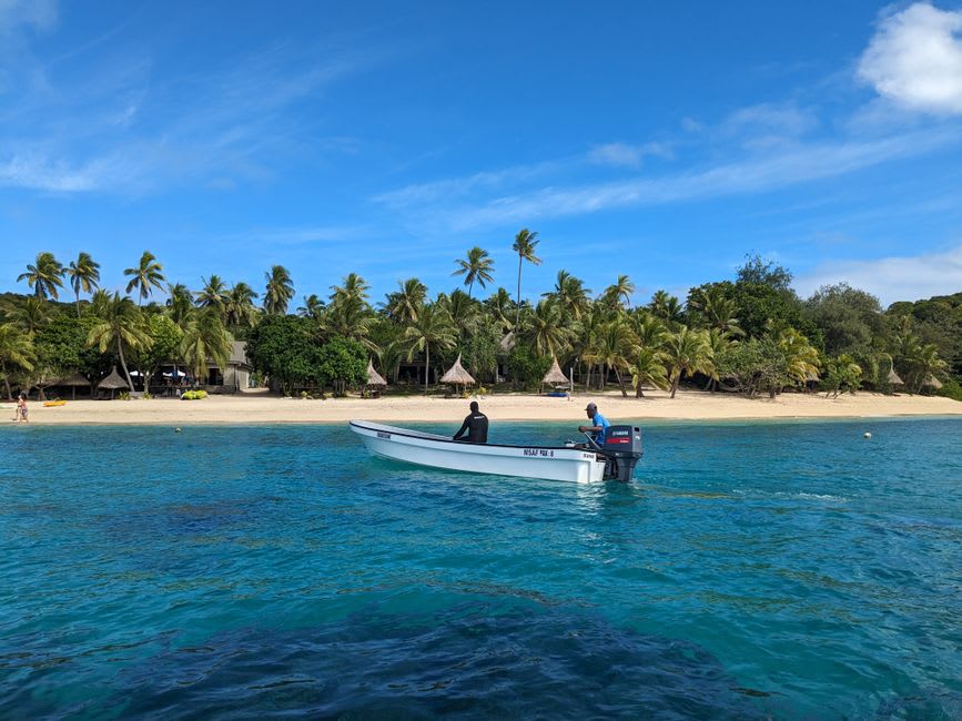 A volleyball net and sand court on Leleuvia island partially submerged by the incoming tide, with palm trees behind
