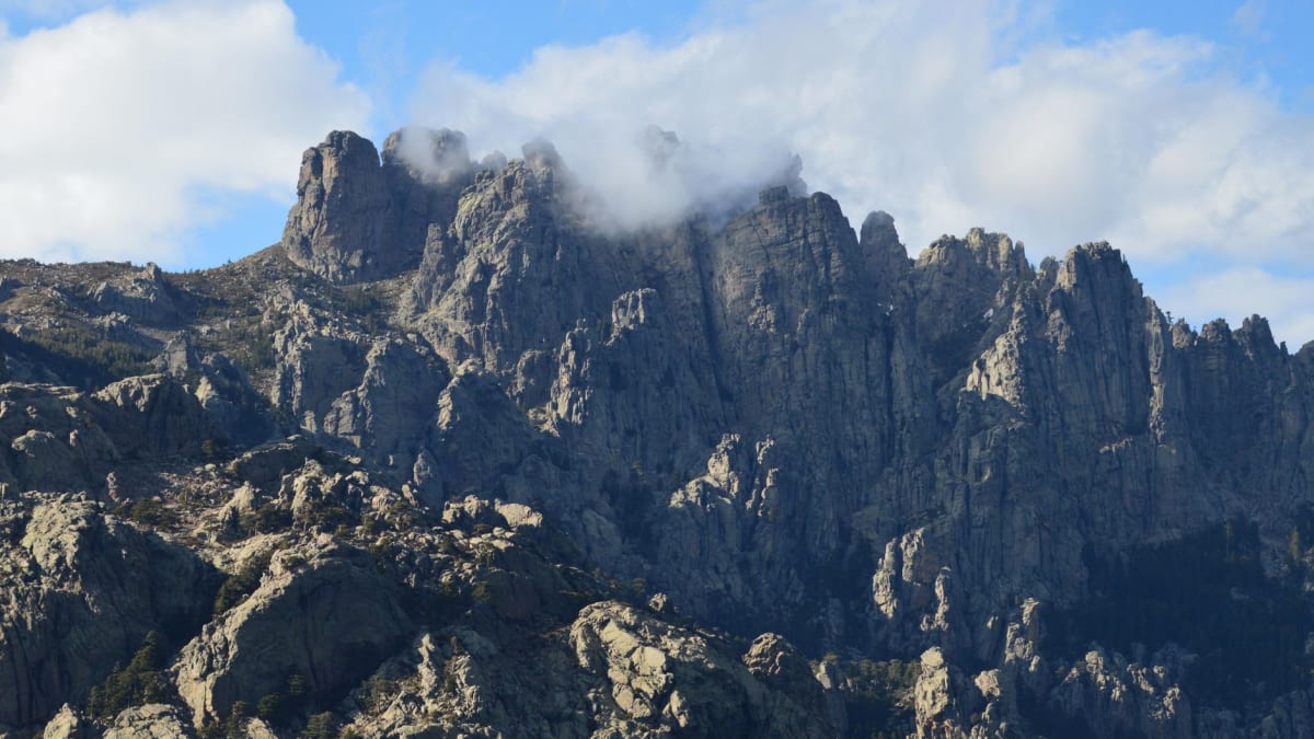 Une piscine naturelle de granit sous les aiguilles de Bavella, des randonneurs se reposant sur la roche environnante réchauffée par le soleil
