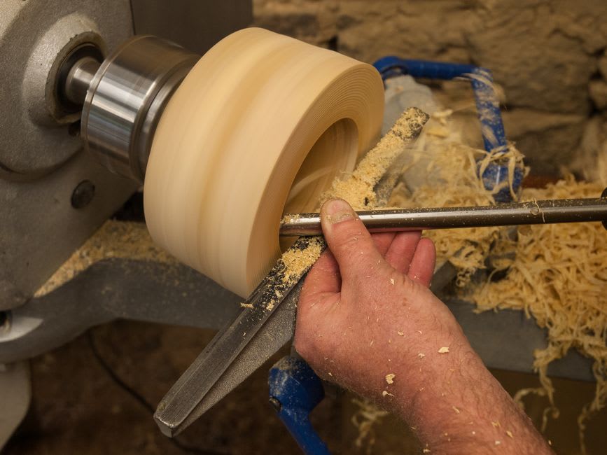 Un tour de tourneur sur bois dans un atelier de Foncine-le-Haut, des boucles de copeaux clairs amoncelées sur le sol