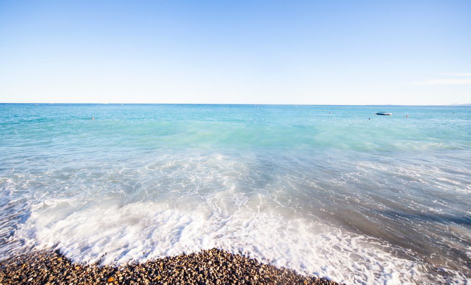 La plage de galets et l'eau turquoise limpide de la baie des Anges à Nice, avec la courbe du littoral visible
