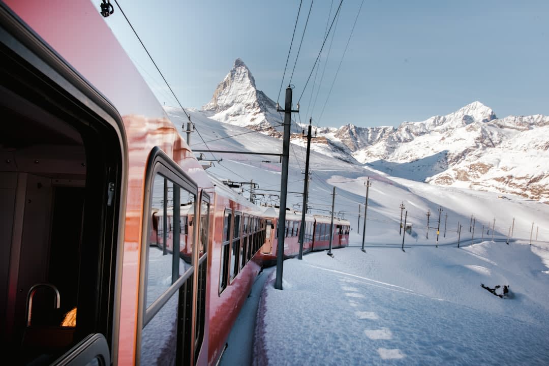 Les wagons rouges du Tramway du Mont-Blanc grimpant au-dessus de la limite des arbres avec des sommets glaciaires au loin