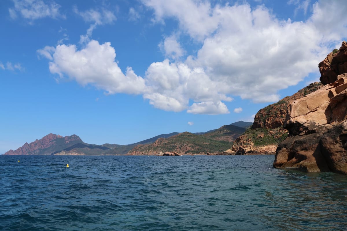 Un bateau dérivant sous des tours de falaises de porphyre rouge dans une crique de Scandola, l'eau d'un bleu-vert profond