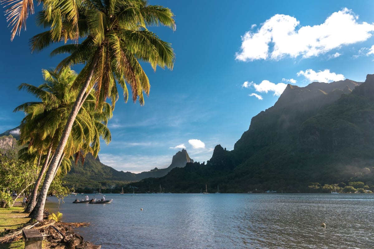 Jagged volcanic peaks of Moorea draped in morning cloud, seen from the water of Cook's Bay with a traditional pirogue in the foreground