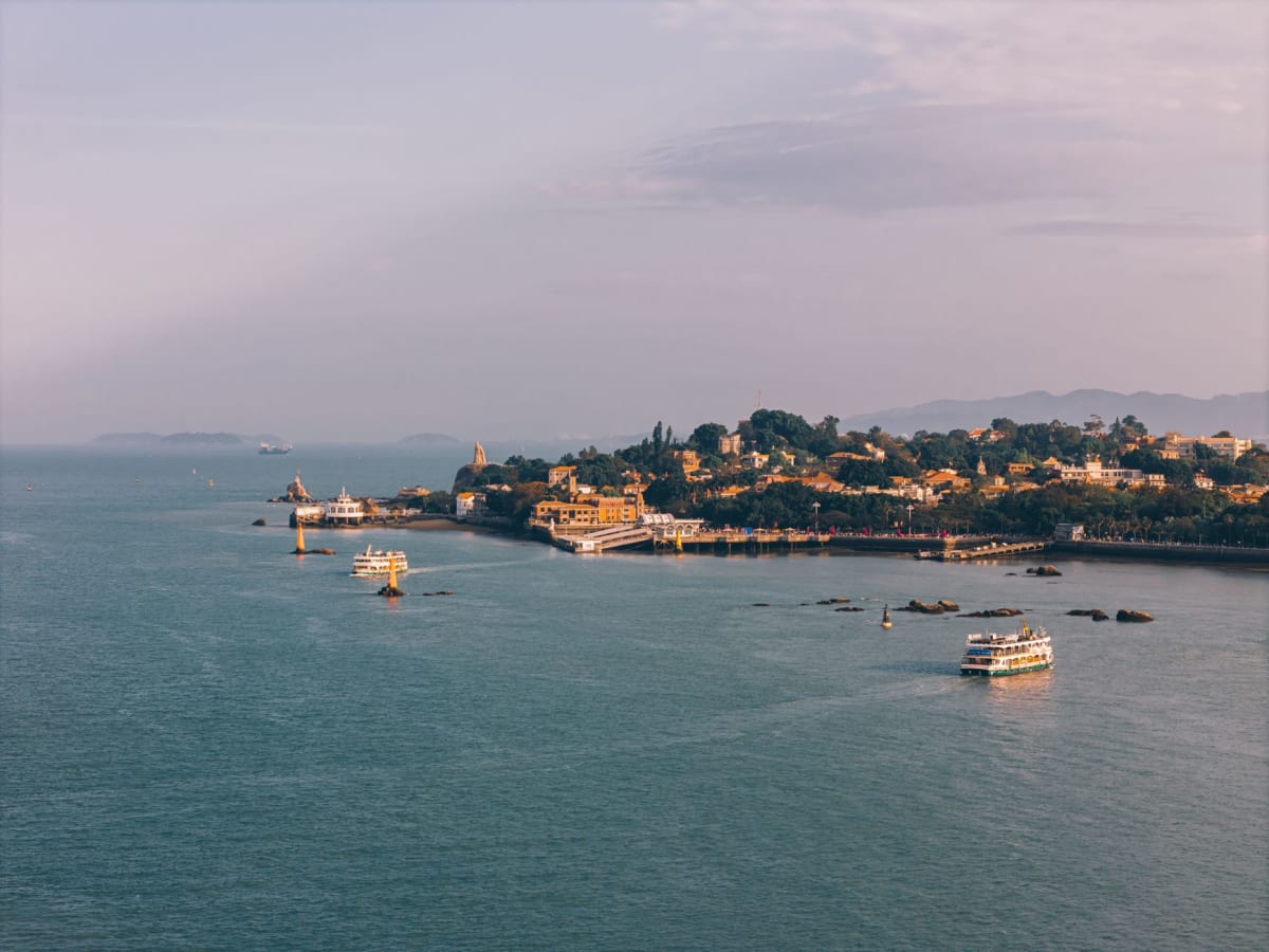 Rocky granite headland on the eastern coast of Meizhou Island with Taiwan Strait waves breaking below, fishing village visible in the distance