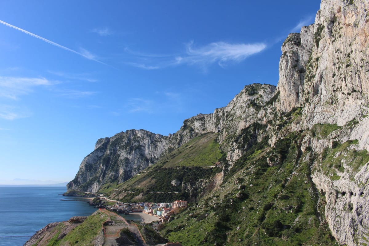 The eastern face of the Rock of Gibraltar seen from Eastern Beach, the vast limestone cliff rising from the shore with late afternoon light turning it golden
