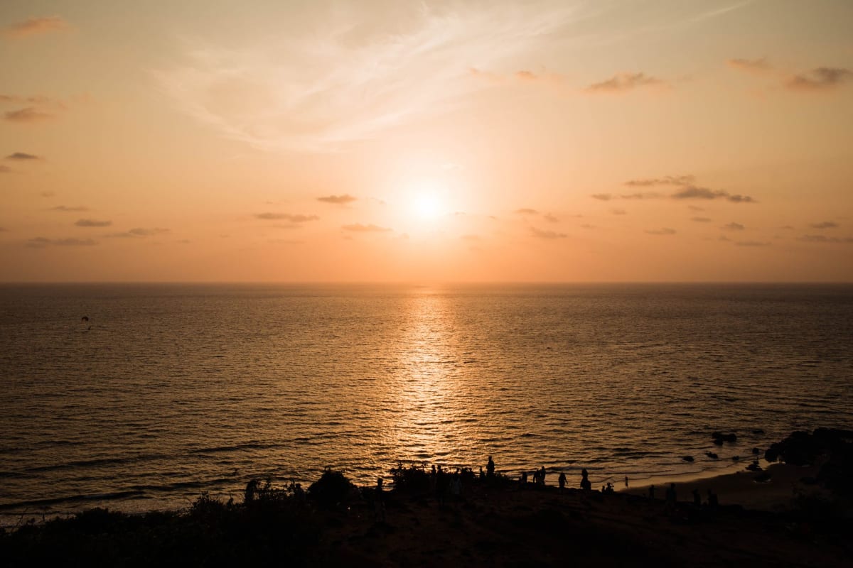 Trois amis assis sur les bastions de latérite rouge du Fort Chapora surplombant le littoral de Goa au coucher du soleil